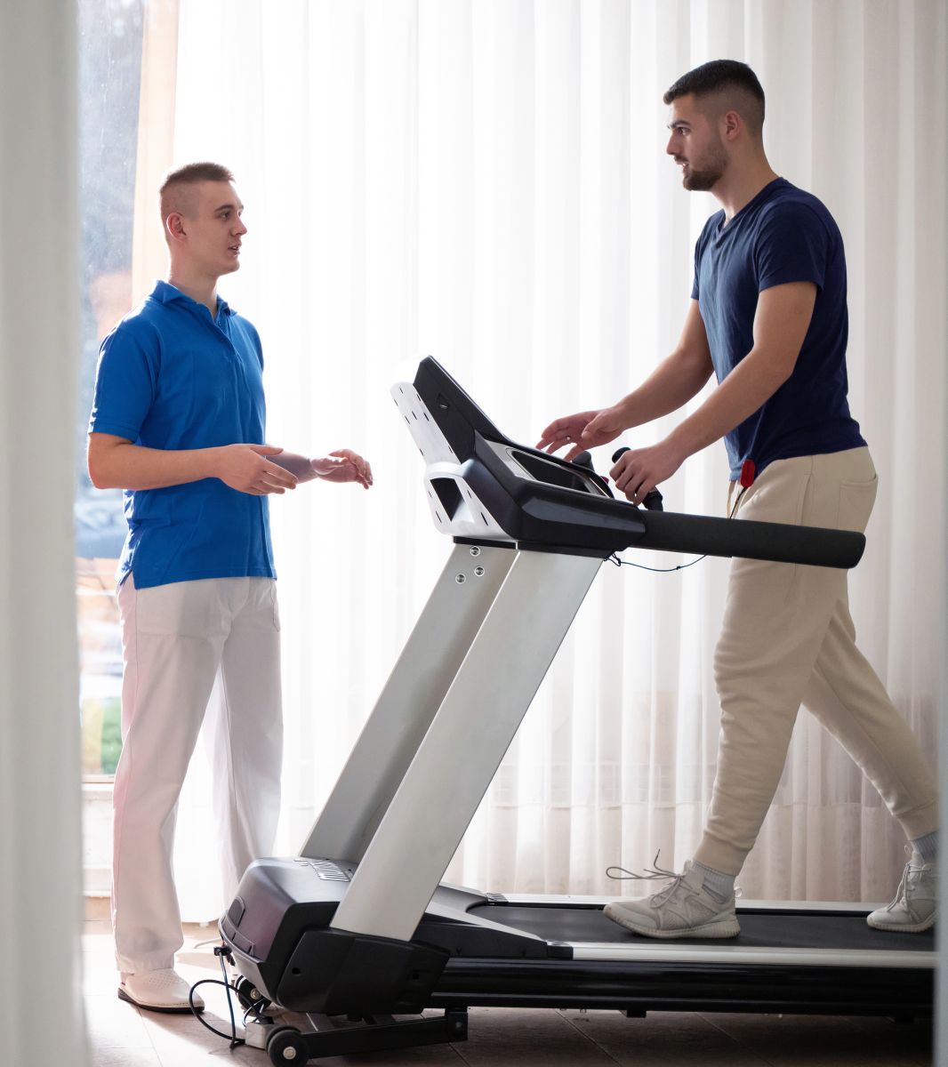Image of man walking on a treadmill next to a Physical Therapist.