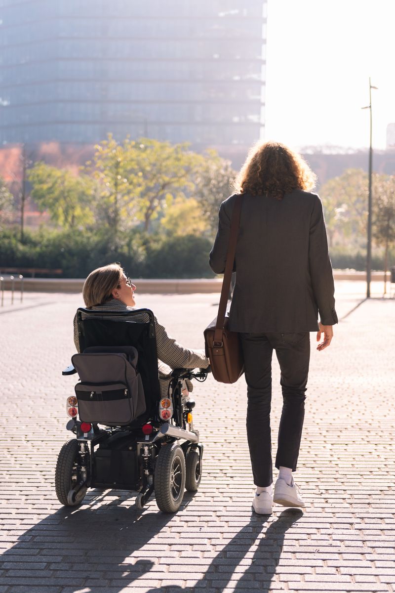 Image of a woman walking alongside a woman in a power wheelchair